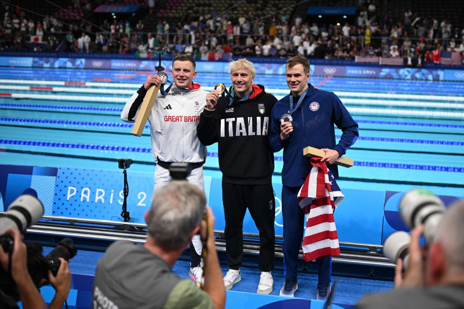 Silver medallists Britain's Adam Peaty (L) and US' Nic Fink (R) and gold medallist Italy's Nicolo Martinenghi celebrate after the men's 100m breaststroke swimming event during the Paris 2024 Olympic Games at the Paris La Defense Arena in Nanterre, west of